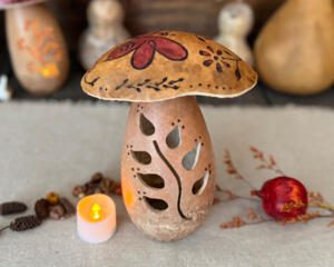This shows a handmade mushroom decoration. Made from a gourd, it has a fern carved in the stock and wood burned bee artwork on top. 